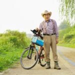Senhor idoso de chapéu com uma bicicleta de cestinha passeando pela estrada