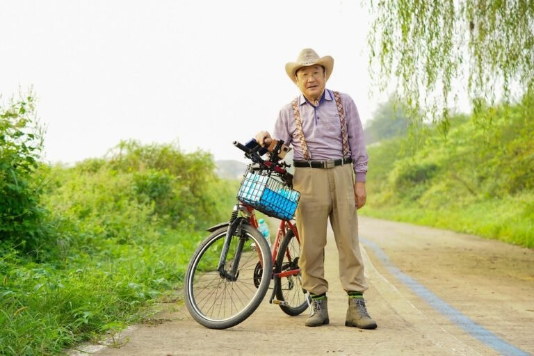 Senhor idoso de chapéu com uma bicicleta de cestinha passeando pela estrada