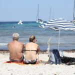 Casal de idosos na praia em baixo de um guarda sol olhando o mar