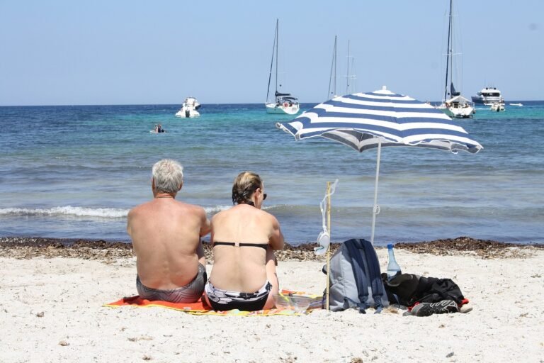 Casal de idosos na praia em baixo de um guarda sol olhando o mar