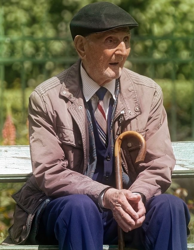 Senhor idoso sentado no banco da praça sozinho