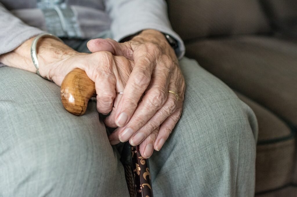 senhor idoso sentado com as mãos apoiadas em uma muleta