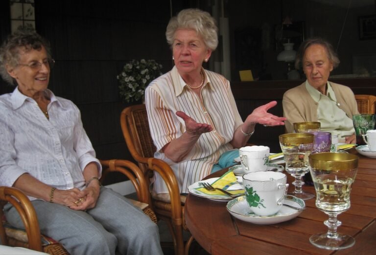 três senhoras idosas sentadas em uma mesa conversando e comendo